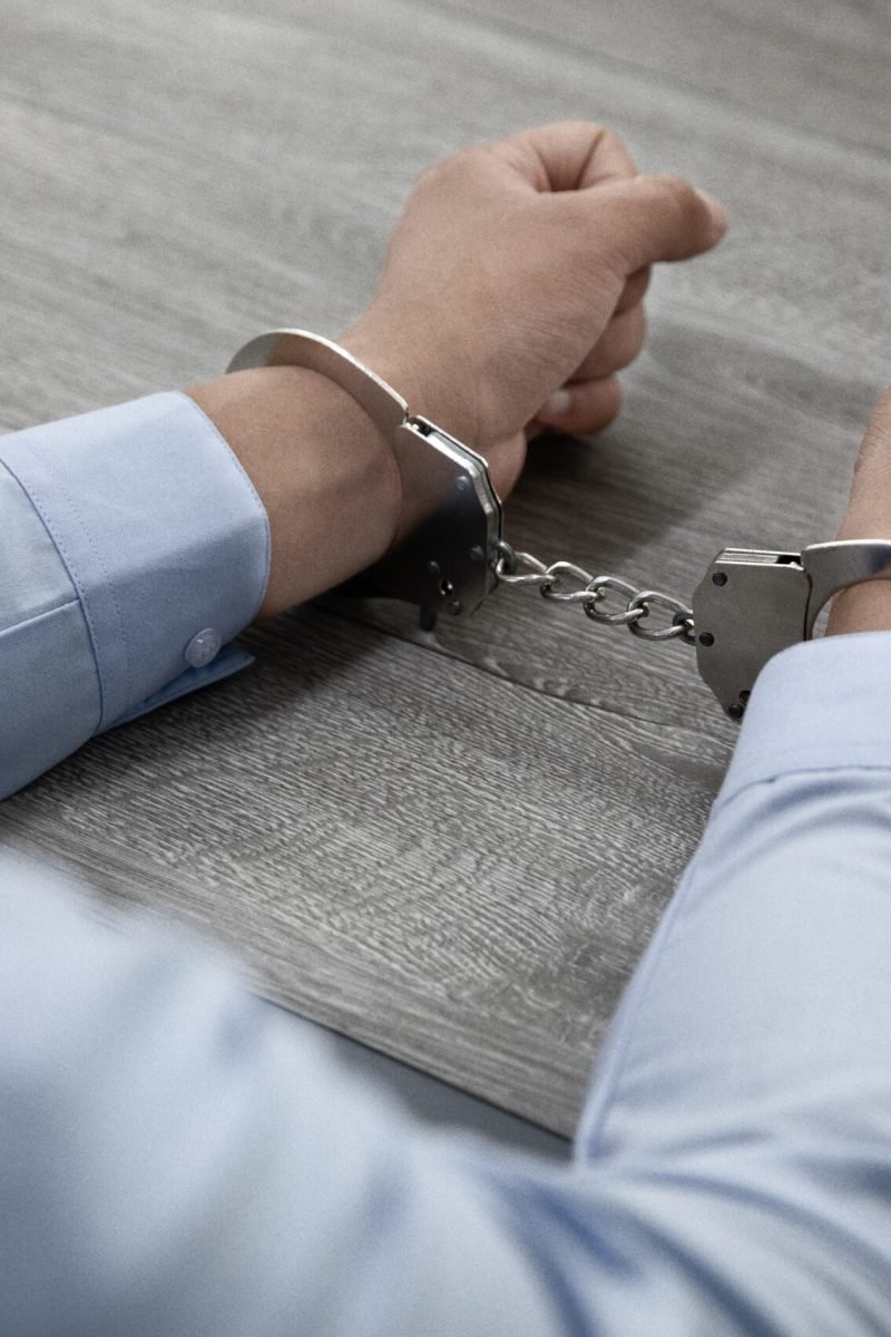 A selective focus shot of male hands in handcuffs on a wooden table